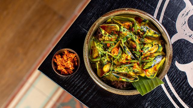 Close up of a dish with muscles in green sauce, on a black wooden table.
