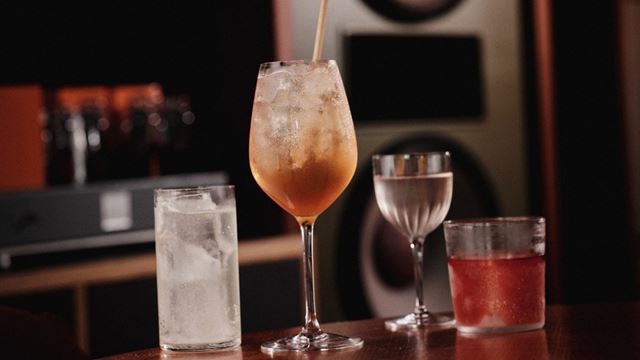 Four cocktails on a wooden table with sound system in the background.