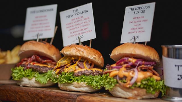 Three beef burgers with cheese, bacon, lettuce, onions and pickles on sale at a street food stall in Borough Market.