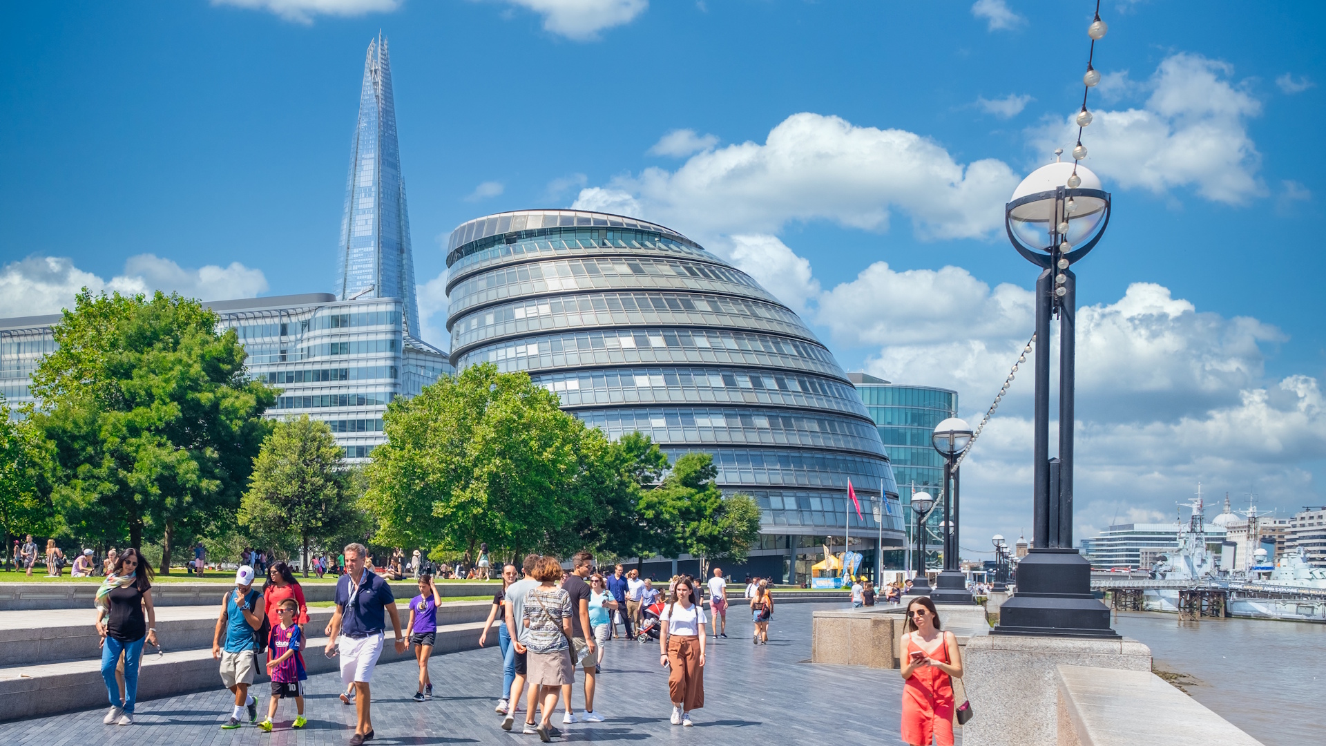 London City Hall and The Shard on a clear sunny day with blue sky and people walking on the riverside path.
