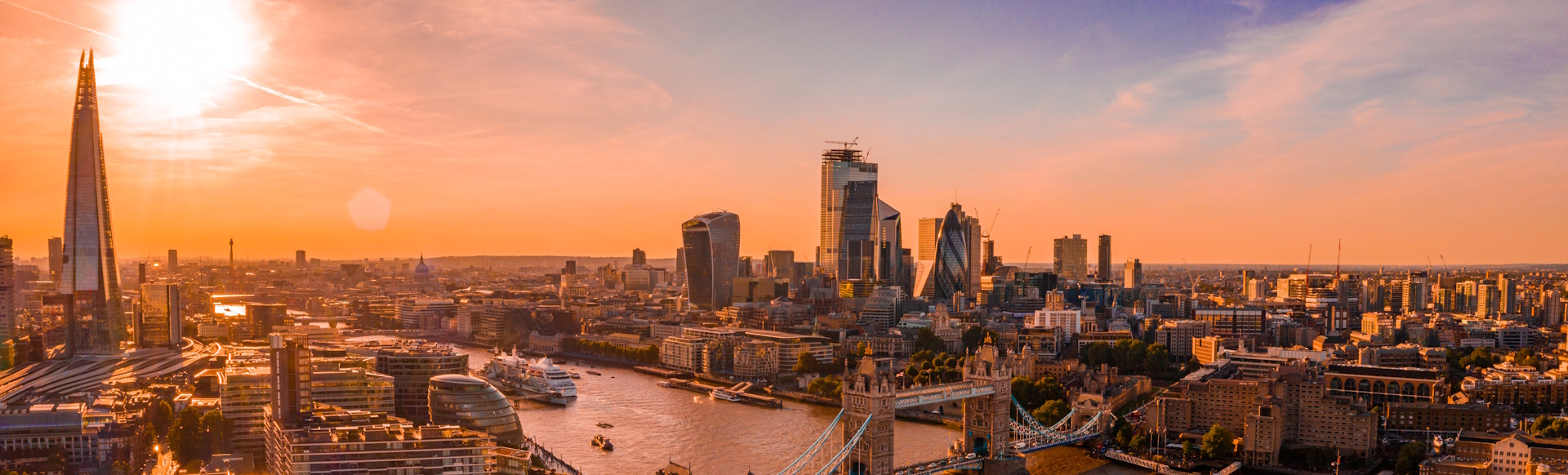 Skyline view of central London at sunset, including iconic buildings such as The Shard, Tower Bridge and the City skyscrapers.