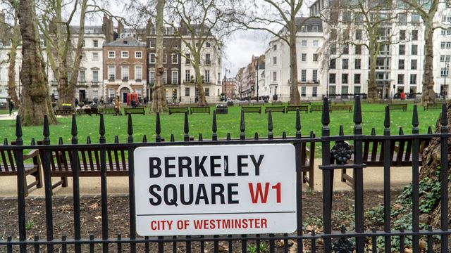 A view of Berkeley Square from in front of its wrought-iron fence, showing the road sign for the square and the green grass of the square behind,