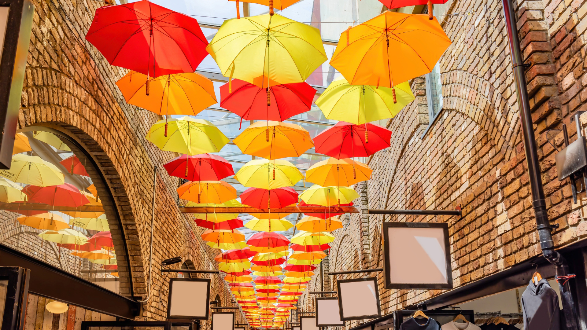 A photo of umbrellas in red, yellow and orange that hang above Camden Market as the sun shines through