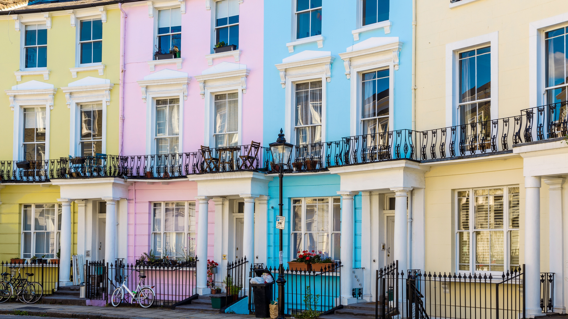A photo of four colourful town houses on Chalcot Square in Camden, painted in a pale yellow, baby pink, bright blue and sherbert orange