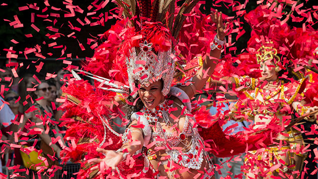 Une reine du carnaval danse au carnaval de Notting Hill © Natasha108 via iStock. Avec l'aimable autorisation de Natasha108 via iStock. Une reine de carnaval vêtue d'un costume blanc avec des plumes rouges, entourée de rubans rouges, danse au carnaval de Notting Hill.