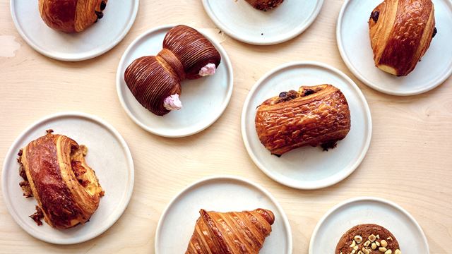 Several plates with pastries including croissants and pains au chocolat on display in white plates on a wooden table.