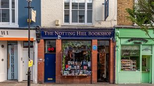 Photo showing the iconic blue and red brick bookshop that appeared in the movie Notting Hill, with green doughnut shop next door.