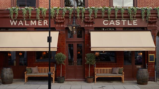 Walmer Castle pub exterior with hanging plants, wooden benches out front and a red-brick building.