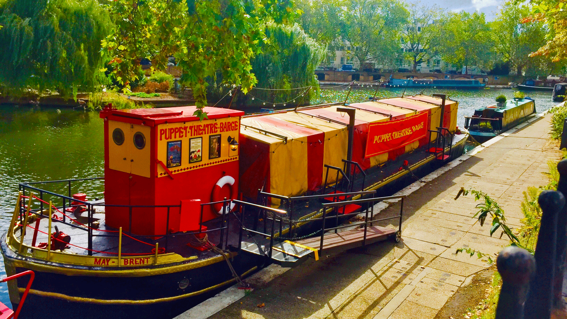 Red and orange barge on the river on a bright sunny day with Puppet Theatre Barge painted on the side