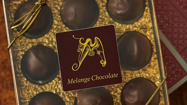 Close up of chocolate box filled with chocolate truffles, with brown and gold label that reads Melange Chocolate.