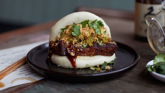 Close up of a pork belly bao bun with sauce, coriander and nuts.