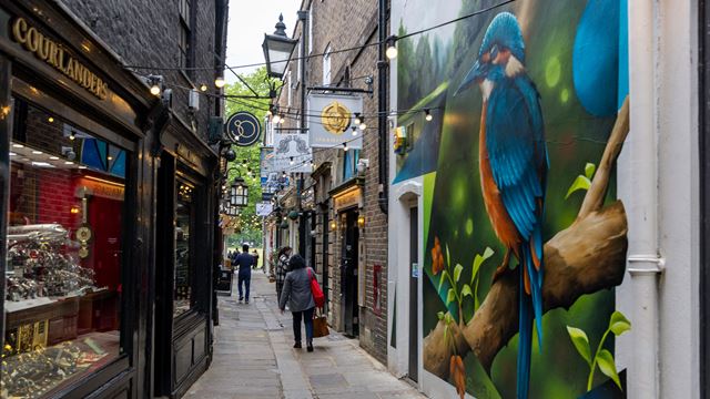 People walking along Brewers Lane in Richmond, with independent shops and a colourful bird mural