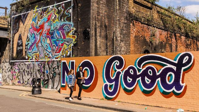 Orange street art featuring the words 'no good' in black cursive font, painted on a brick wall in Hackney.