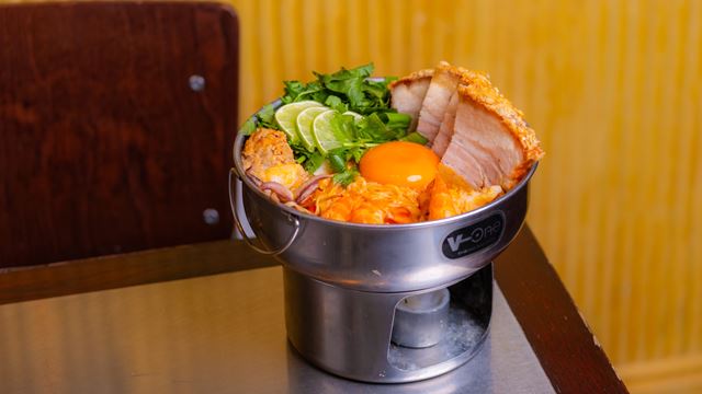 Close up of a Thai dish with an egg, fried chicken, pork, salad and lime in a big bowl.