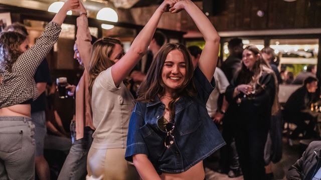 people smiling and dancing in an irish themed traditional bar, with people stood around holding drinks