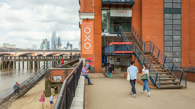 exterior shot of Oxo Tower Wharf, with people walking towards it and people on the beach as the river Thames tide is out