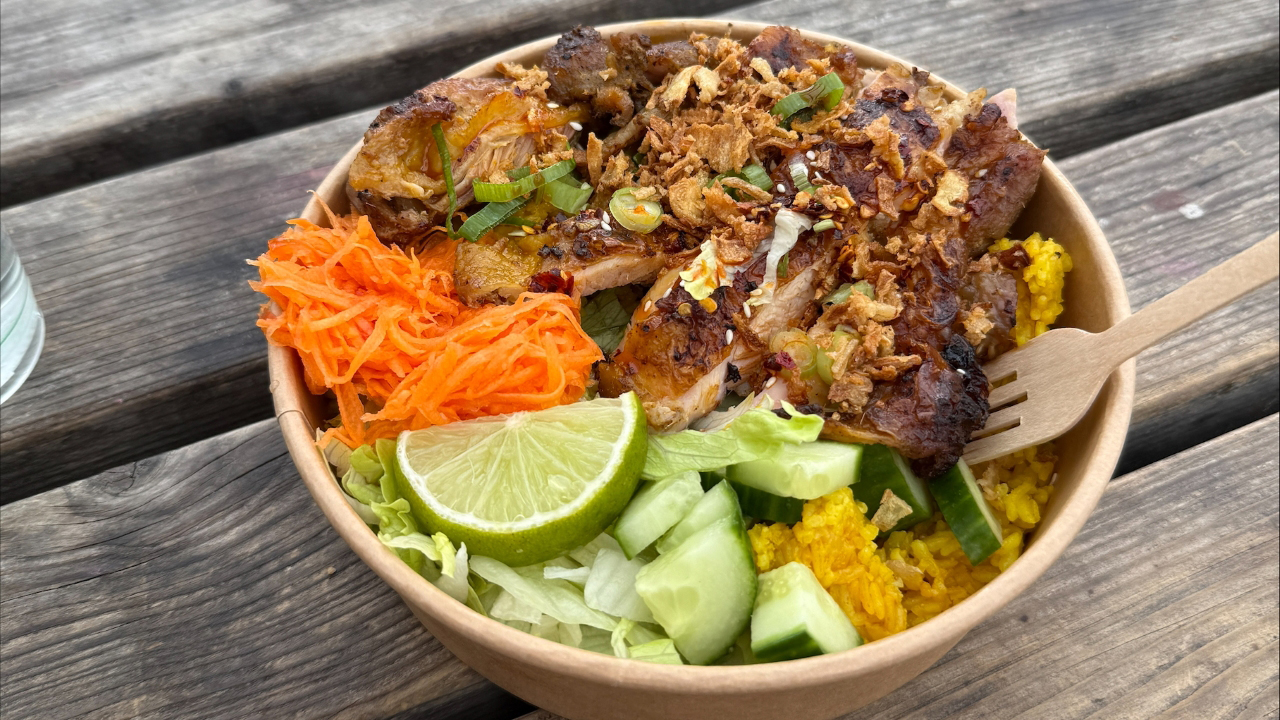 A photo of a Filipino rice and chicken bowl with cucumber, salad, grated carrot and a wedge of lime with spring onion and crispy onions topping the chicken