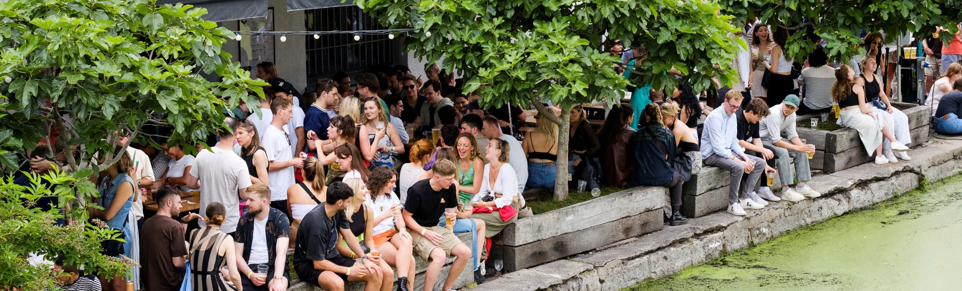 A photo of crowds of people smiling and enjoying the sunshine along the canal in front of Crate Brewery in Hackney Wick