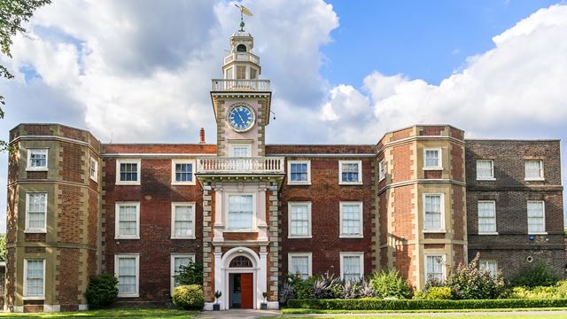 Red-brick facade of Bruce Castle Museum with clock tower and blue skies with clouds.