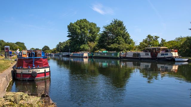 Stonebridge Lock with canal boats and trees on a sunny day with blue sky.