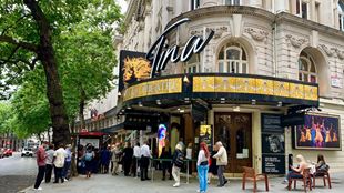 The exterior of the Aldwych Theatre in London, with big letters spelling out Tina above the entrance, people waiting outside and trees alongside the building.