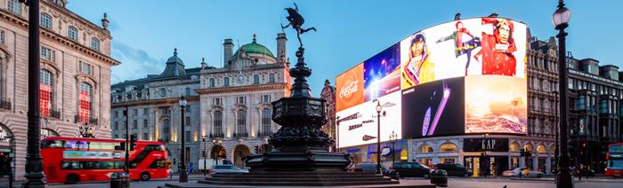 Eros statue and advertising screens at Piccadilly Circus in London's West End, with iconic red London bus driving past.