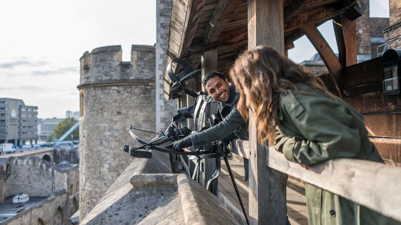 Imagine what it was like to live inside the Tower of London as you walk along the fortifications. Credit: Michael Barrow. Image courtesy of London & Partners. Two people stand on the stone battlements next to a crossbow on the tower of london.