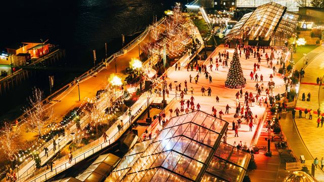 Aerial view of the Battersea Power Station ice rink with a riverside trail, a glass-panelled marquee and a central Christmas tree.