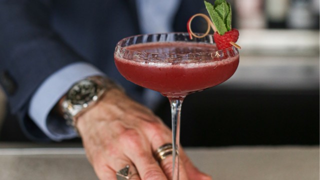 Atelier cocktails avec Gordon Ramsay. Image fournie par Red Letter Days. Homme en costume plaçant un cocktail rouge décoré d'une framboise sur un bâton à cocktail.