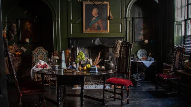 A dark wooden table laid with fruits, candles and feathers inside Dennis Severs' House in London, with paintings on the walls and dark wood floorings.