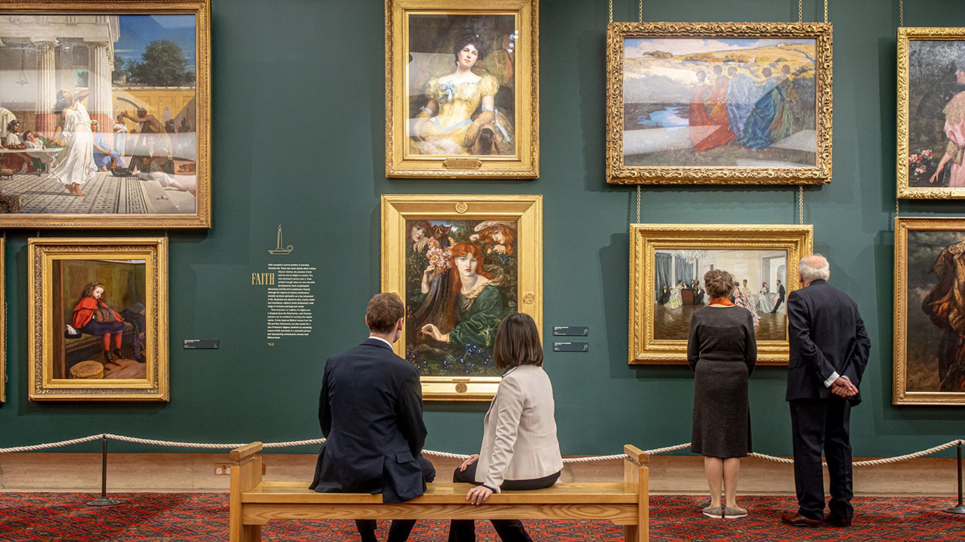 Two people sitting and two other people standing in front of paintings at Guildhall Art Gallery.