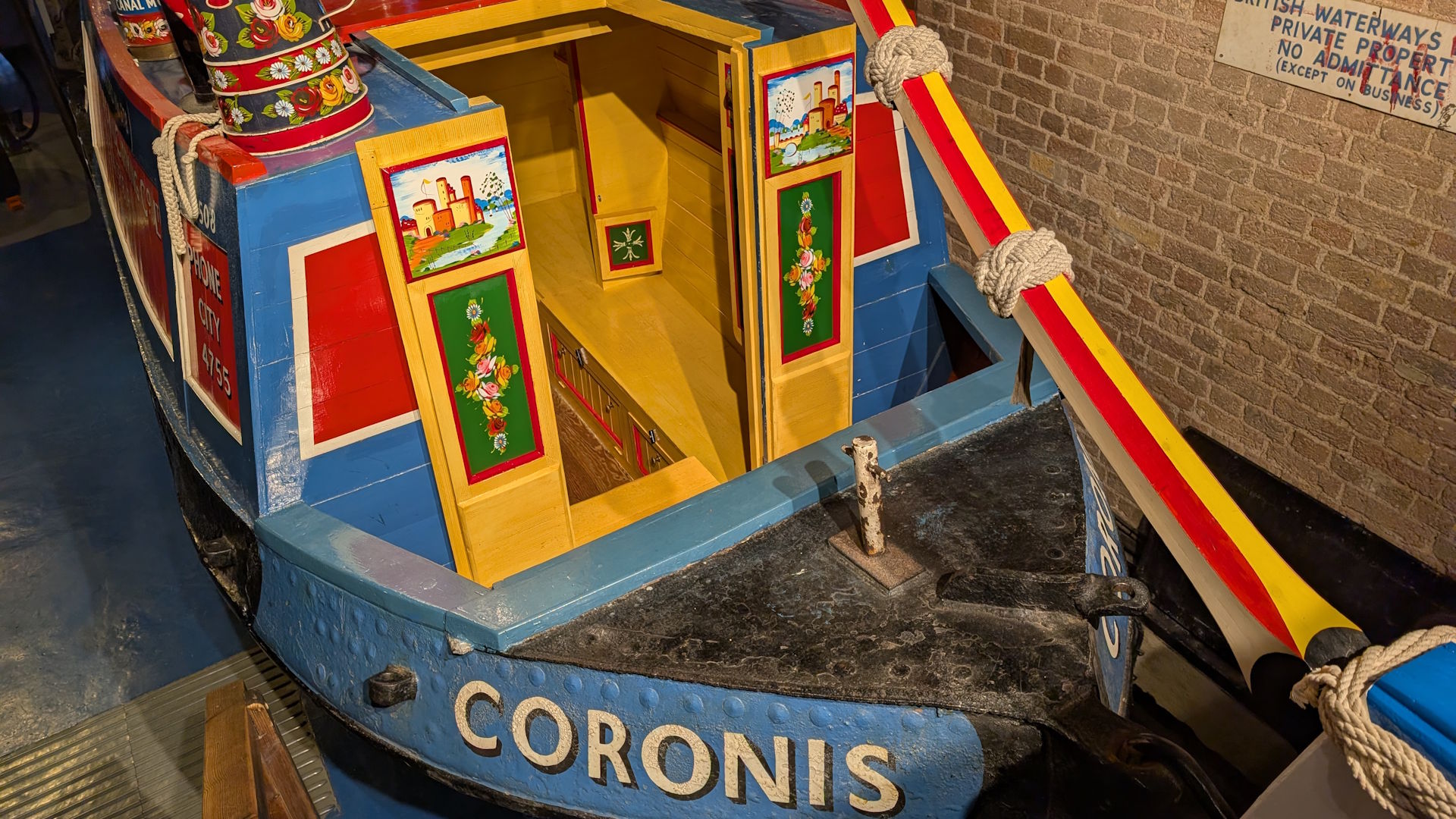 A coloufully painted canal boat in blue red, yellow and green, with the name "Coronis" painted on the side. 