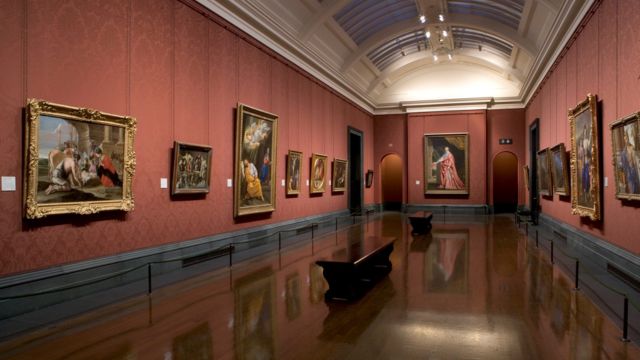 A red exhibition room where walls are lined with paintings at the national gallery in london.