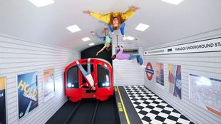 Group of people posing within an illusion that looks like they're hanging upside down in a London tube station.