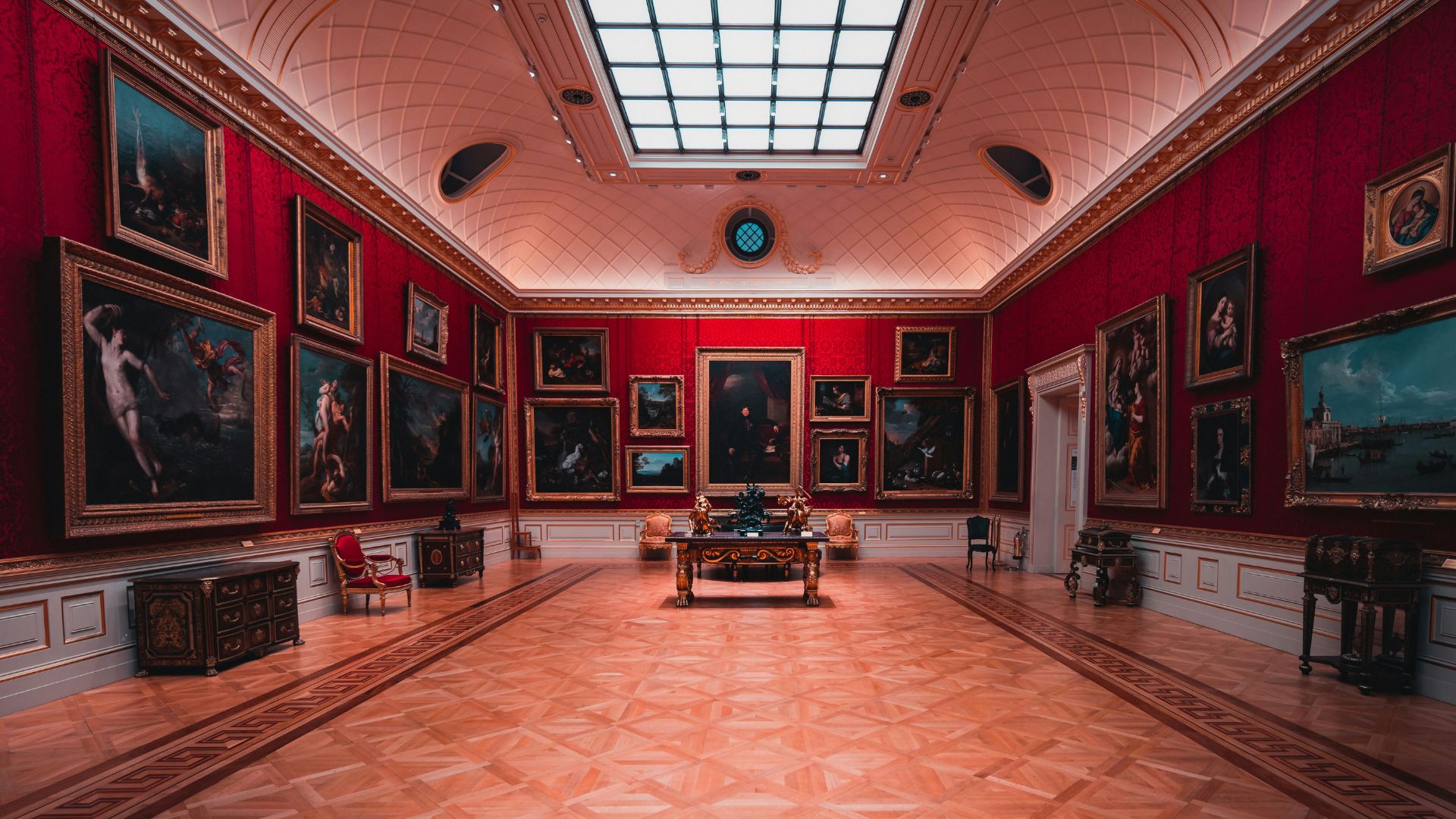 View of The Wallace Collection gallery with red walls and paintings displayed on each.