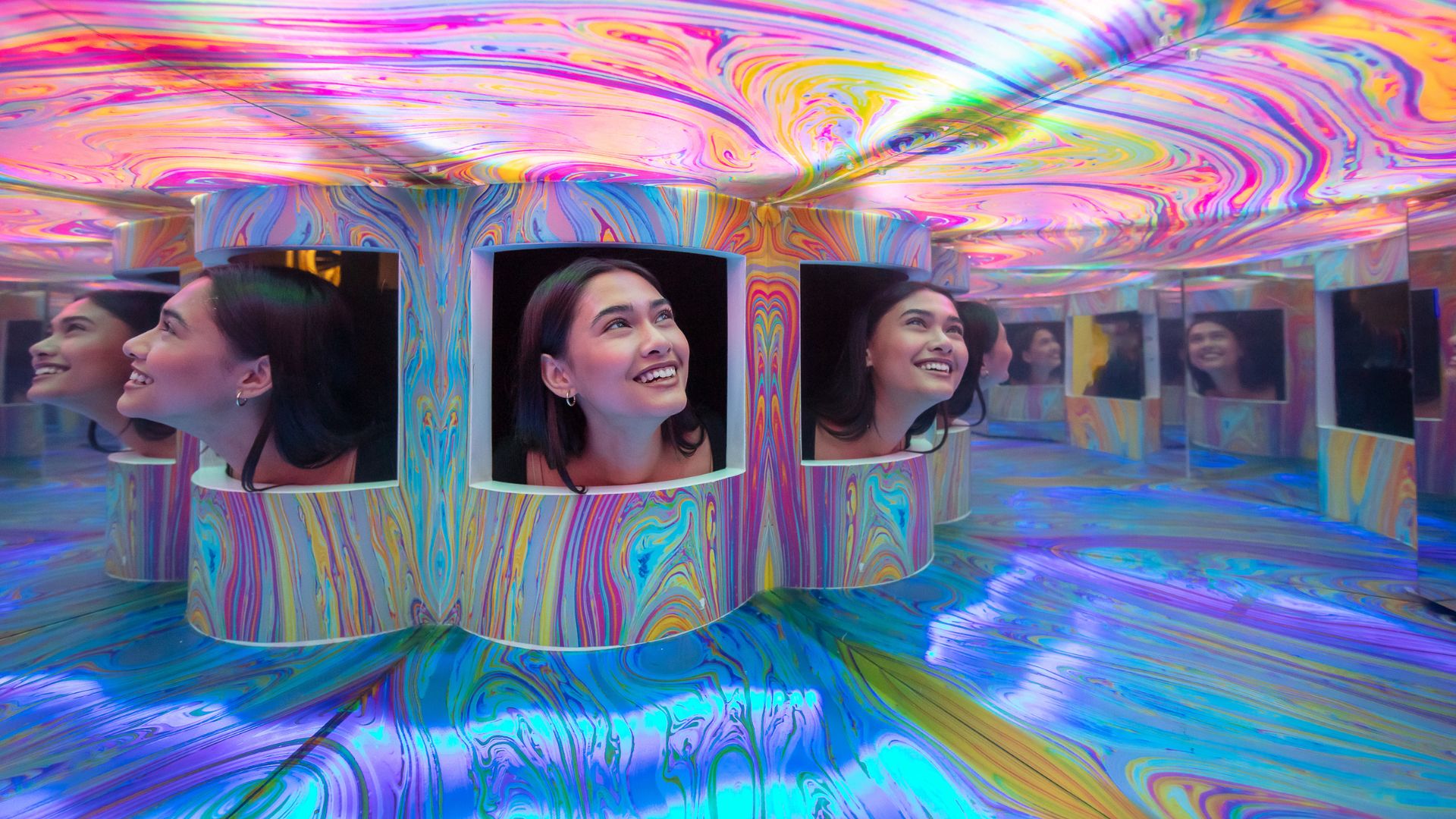 Person looking into colourful mirrored illusion room at Twist Museum.