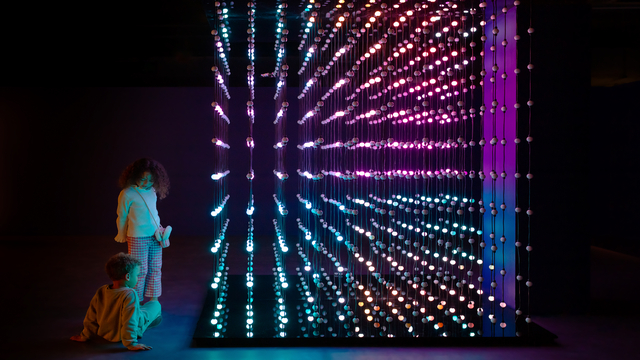 Zwei Personen sitzen neben einer bunten Lichtinstallation in einem dunklen Raum im Twist Museum in der Oxford Street.