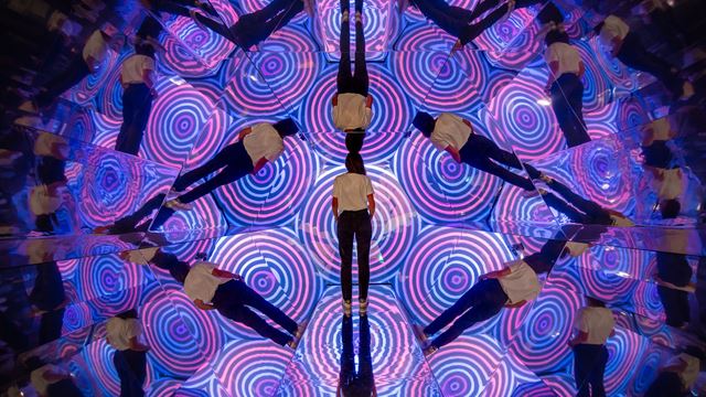 Un homme se tient devant une illusion d'optique au Twist Museum : un kaléidoscope de couleurs violettes et roses et de multiples versions de lui-même.