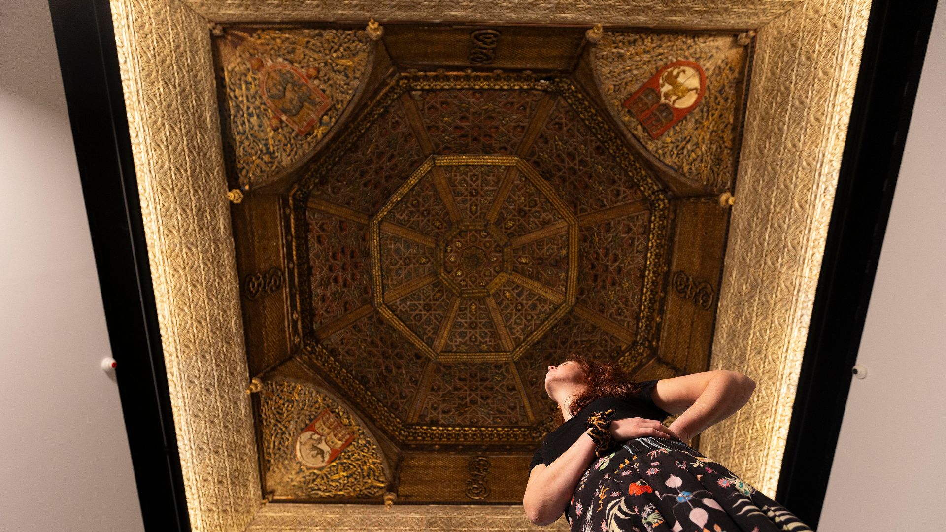 A woman looks up at an intricately designed wooden ceiling.