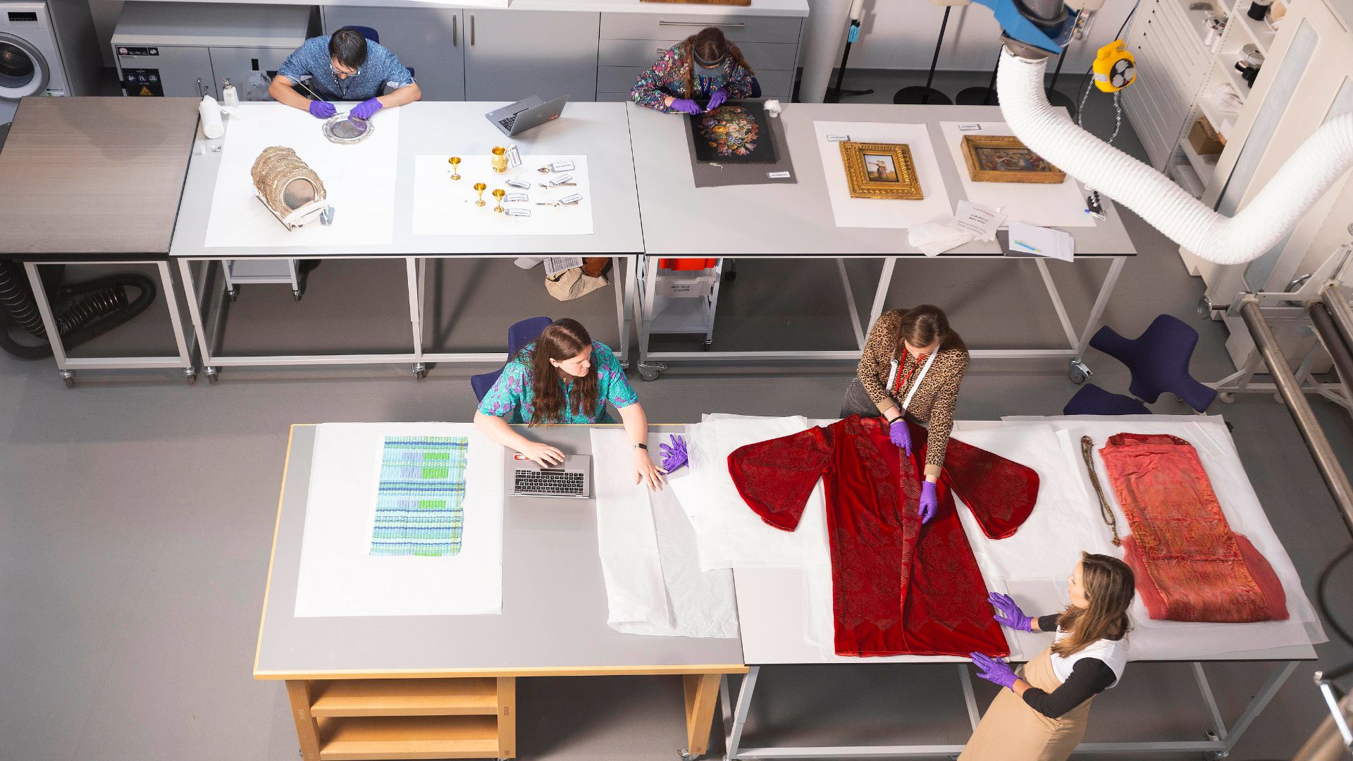 Multi-purpose conservation studio, visible by the Conservation Overlook, at V&A East Storehouse. Image courtesy of V&A. Photo credit: David Parry, PA Media Assignments Large white tables with artefacts being worked on by museum conservation specialists.