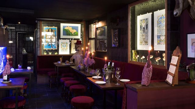 A dimly lit bar at The Viktor Wynd Museum of Curiosities, featuring a lion in a top hat, bar stools and quirky exhibits on the wall.