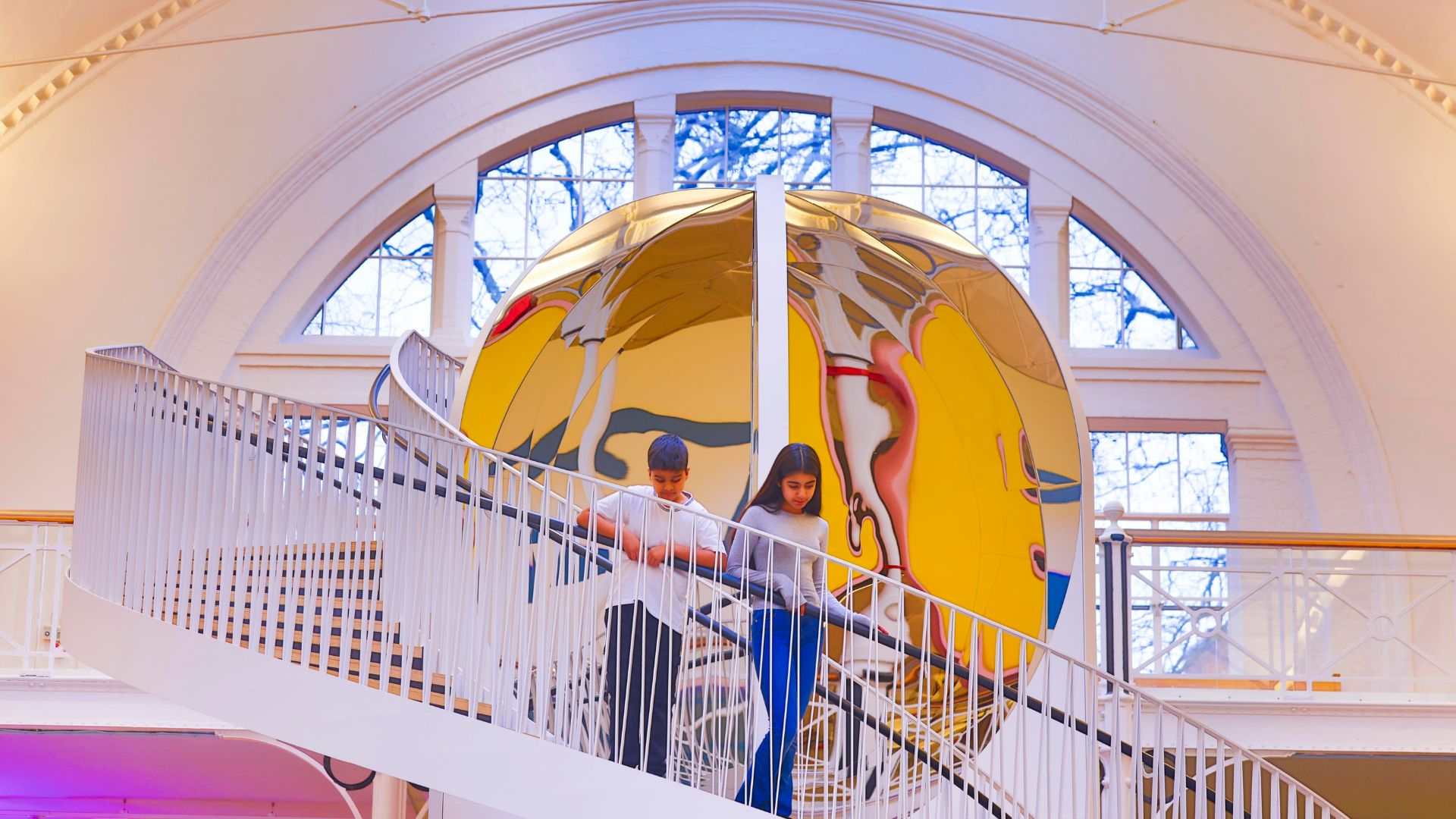 Children walking down a spiral staircase beside a mirrored installation inside Young V&A, London.