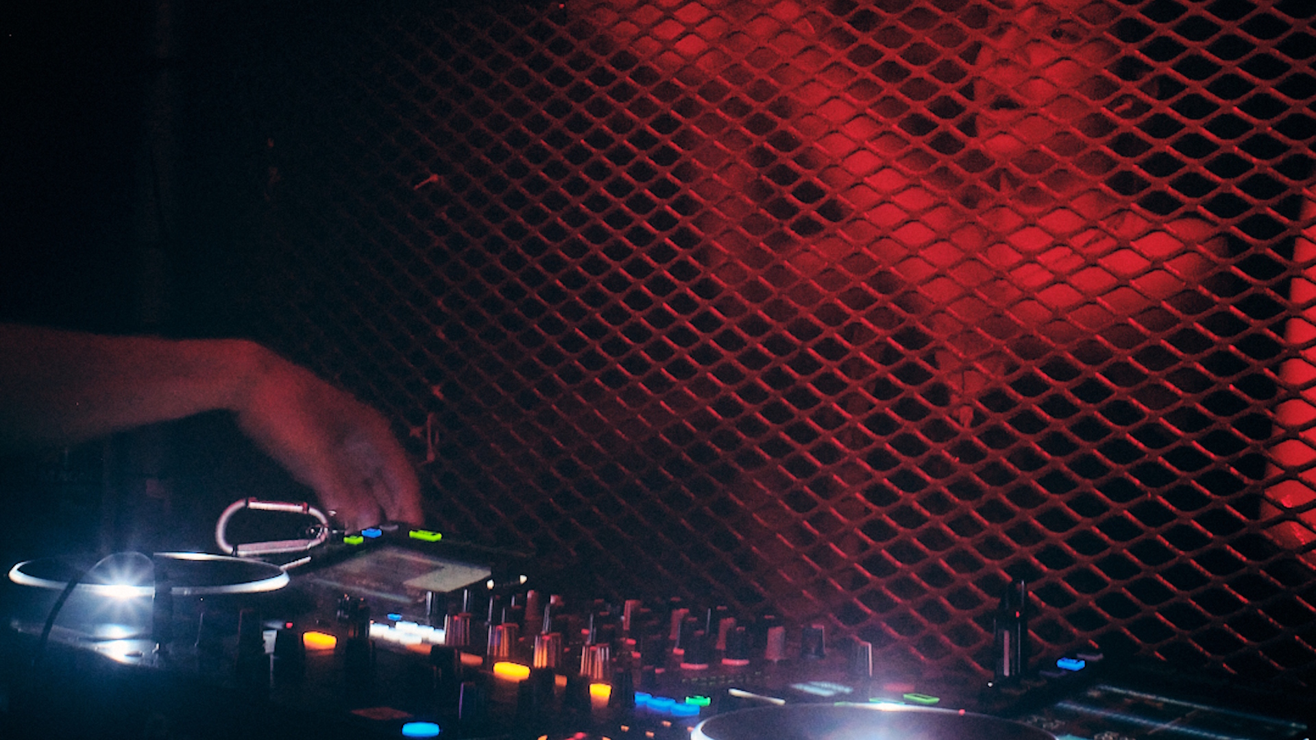Close-up of a DJ booth with woman dancing under red lighting in front of the booth.