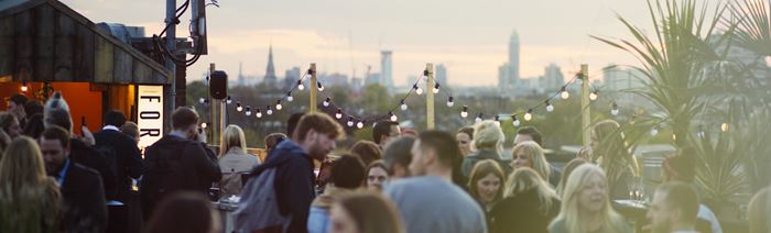 People enjoying a rooftop terrace in summer with views of central London in the distance.