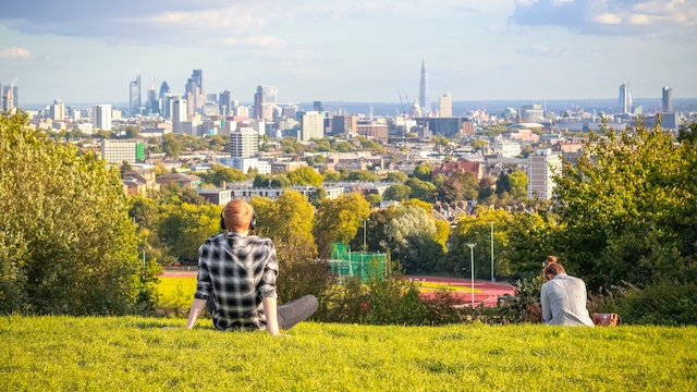 People sitting on Parliament Hill in Hampstead Heath looking at the view of London on a sunny day.