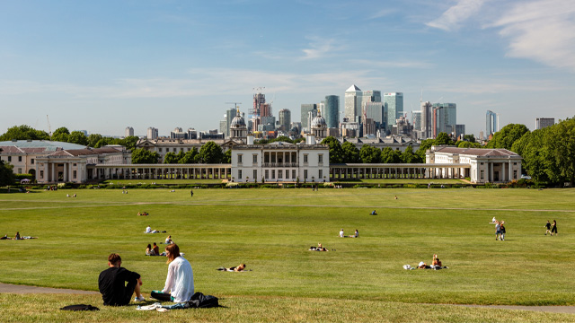 People sitting on the grass in Greenwich Park with the skyline in the distance.