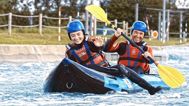 Hot Dog Kayaking im Lee Valley White Water Centre, Bild von Red Letter Days Eine Frau und ein Mann fahren mit einem Kayak den Fluss am Lee Valley Water Centre entlang.