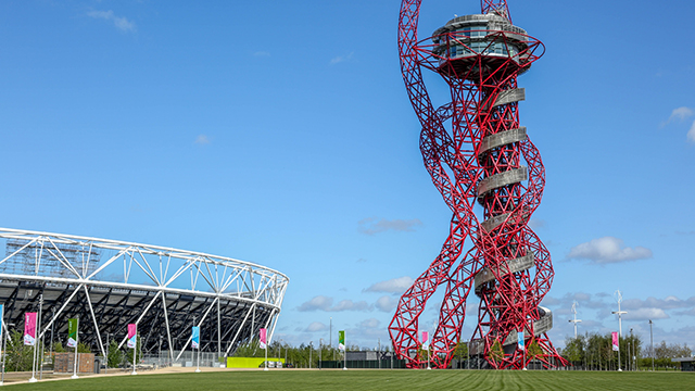 Die rote, gewundene Struktur des ArcelorMittal Orbit auf der rechten Seite und das Londoner Stadion auf der linken Seite, an einem hellen Tag.