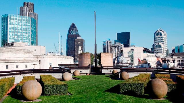 A beautifully landscaped rooftop terrace overlooks London's gherkin and skyscrapers on a sunny day.