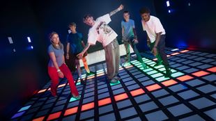 Five people in the Megagrid game room standing on a grid of coloured lights with some squares lit up.